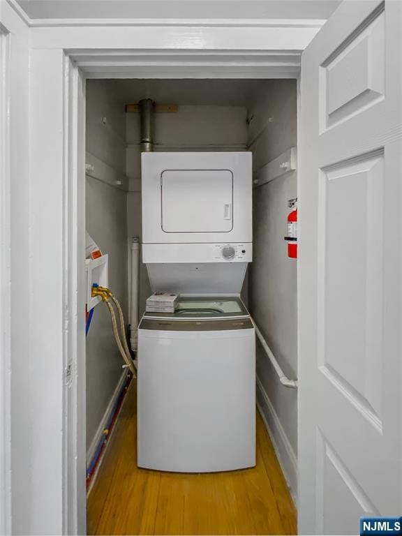 clothes washing area featuring stacked washer and clothes dryer, laundry area, and light wood finished floors