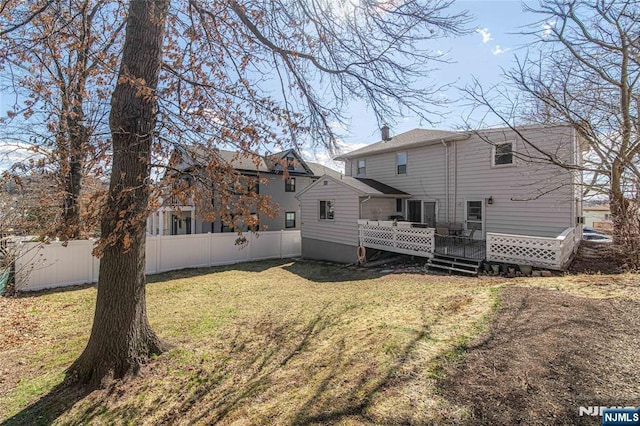 rear view of property with a chimney, a wooden deck, a yard, and fence