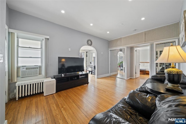 living room with cooling unit, arched walkways, radiator, and light wood-style flooring