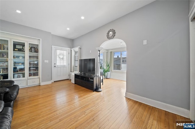 living area featuring baseboards, arched walkways, a healthy amount of sunlight, and light wood finished floors