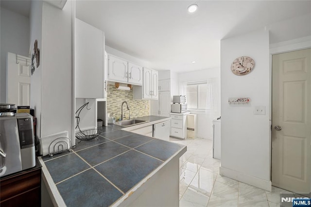 kitchen with marble finish floor, a sink, tasteful backsplash, a peninsula, and white cabinets