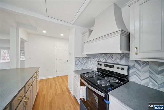 kitchen featuring tasteful backsplash, premium range hood, dark stone counters, light wood-type flooring, and stainless steel range with electric cooktop