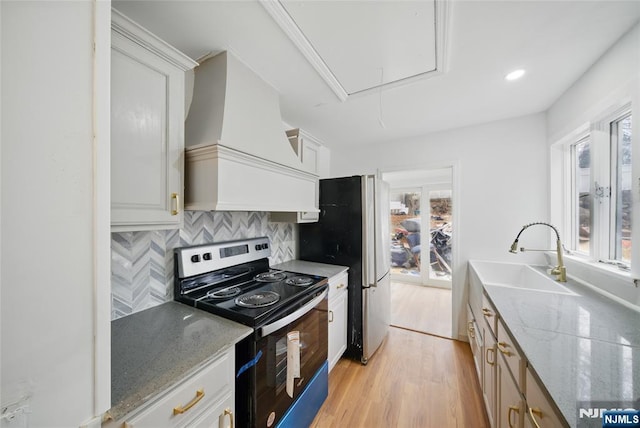 kitchen with premium range hood, light wood-style flooring, a sink, appliances with stainless steel finishes, and decorative backsplash