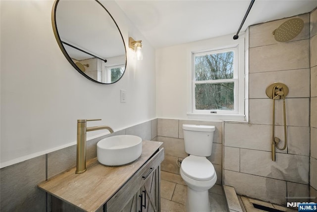 bathroom with vanity, tiled shower, tile patterned flooring, tile walls, and toilet