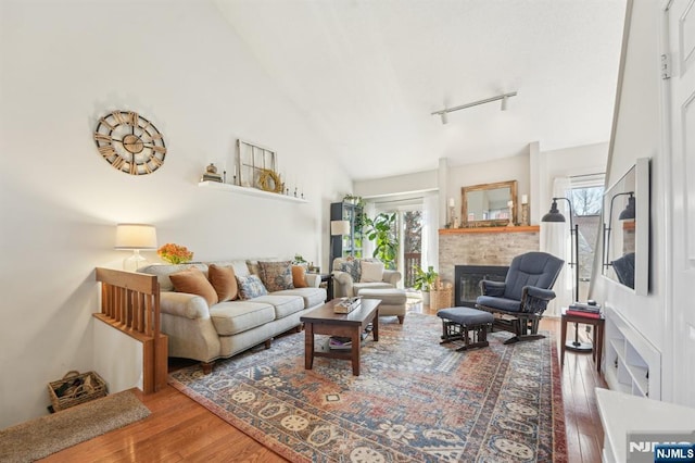 living area with hardwood / wood-style floors, a glass covered fireplace, rail lighting, and high vaulted ceiling