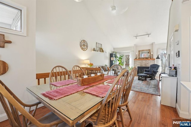 dining room with rail lighting, high vaulted ceiling, light wood-style flooring, and a fireplace