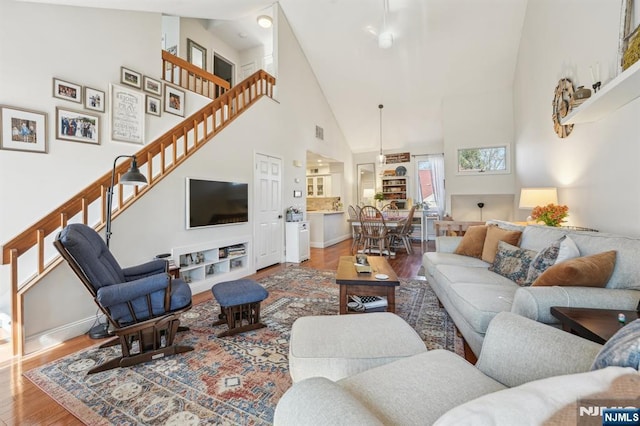 living area featuring stairway, wood finished floors, baseboards, and high vaulted ceiling