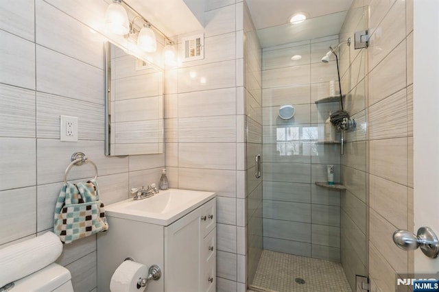 bathroom with visible vents, toilet, vanity, a stall shower, and tile walls