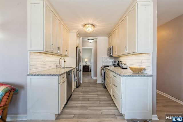 kitchen with light wood-style flooring, a sink, light stone counters, stainless steel appliances, and baseboards