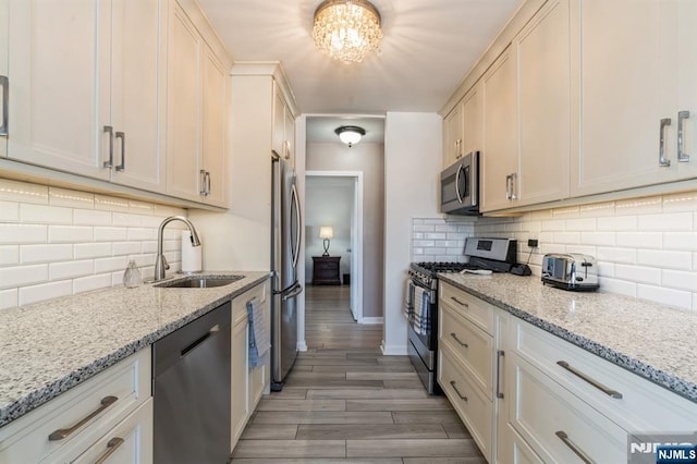 kitchen with light wood-style flooring, a sink, decorative backsplash, appliances with stainless steel finishes, and a notable chandelier