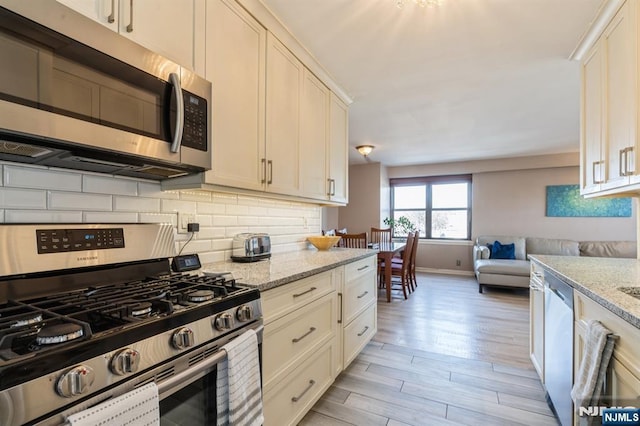 kitchen with light stone counters, light wood finished floors, appliances with stainless steel finishes, open floor plan, and backsplash