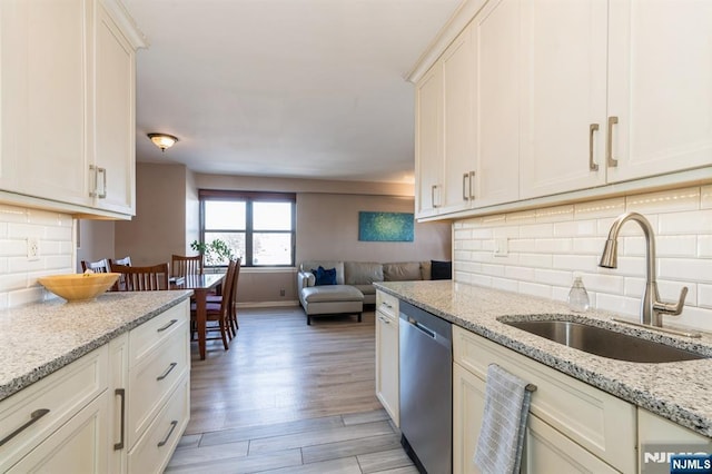 kitchen featuring light wood-type flooring, a sink, backsplash, open floor plan, and dishwasher