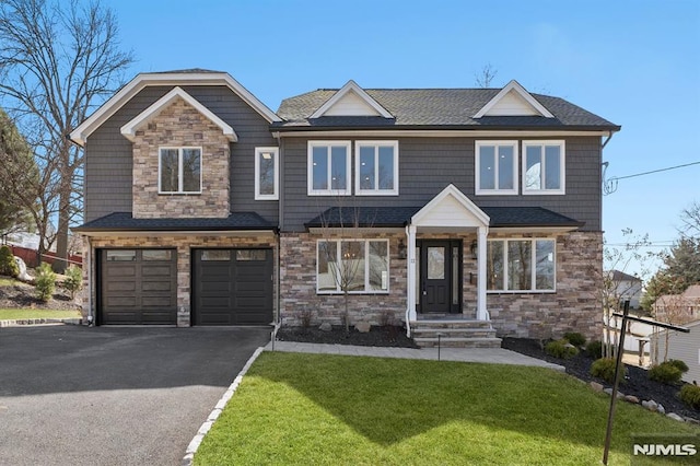 view of front of house featuring roof with shingles, a front lawn, a garage, stone siding, and aphalt driveway