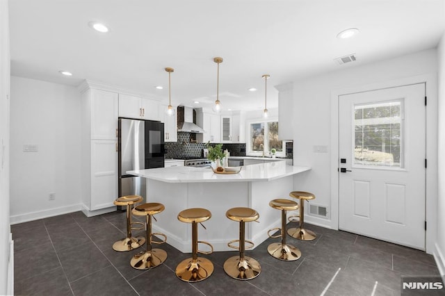 kitchen with visible vents, wall chimney range hood, a peninsula, plenty of natural light, and white cabinets