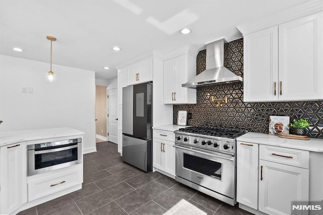 kitchen featuring appliances with stainless steel finishes, white cabinetry, decorative light fixtures, wall chimney exhaust hood, and tasteful backsplash