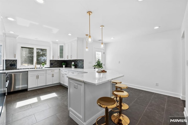 kitchen with backsplash, a peninsula, a kitchen breakfast bar, white cabinetry, and stainless steel dishwasher