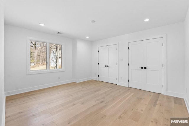 unfurnished bedroom with recessed lighting, light wood-style floors, baseboards, and two closets