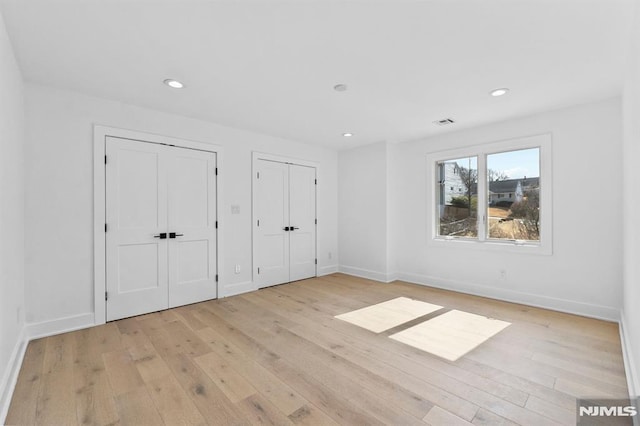 unfurnished bedroom featuring recessed lighting, light wood-style floors, baseboards, and two closets