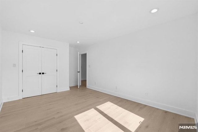 unfurnished bedroom with recessed lighting, light wood-type flooring, a closet, and baseboards