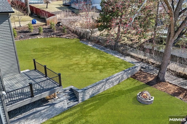 view of yard featuring a wooden deck, a fire pit, and fence