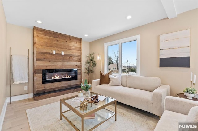 living area featuring a glass covered fireplace, recessed lighting, baseboards, and wood finished floors