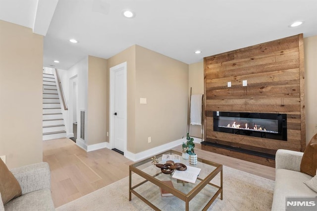 living area featuring a glass covered fireplace, wood finished floors, recessed lighting, stairway, and baseboards