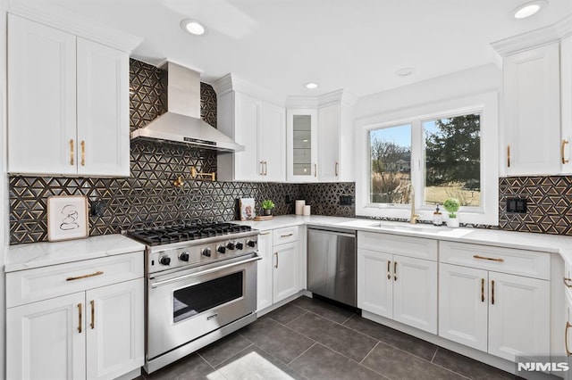 kitchen with a sink, stainless steel appliances, wall chimney exhaust hood, and white cabinets