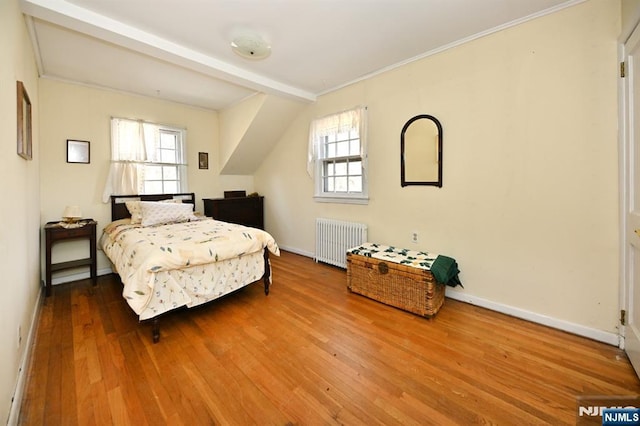 bedroom featuring multiple windows, radiator heating unit, wood finished floors, and baseboards