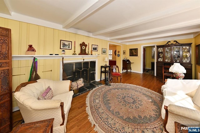 living room featuring beam ceiling, a fireplace with raised hearth, and wood finished floors