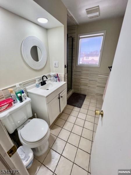 bathroom featuring tile patterned flooring, a shower stall, tile walls, toilet, and vanity