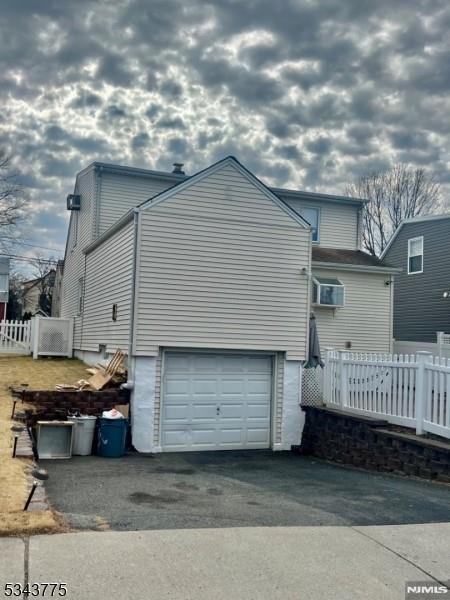 rear view of house featuring driveway, a garage, and fence