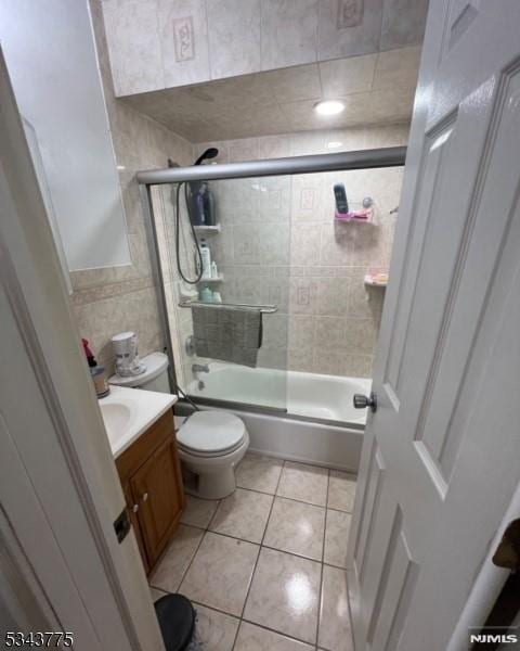 bathroom featuring tile patterned floors, toilet, tile walls, bath / shower combo with glass door, and vanity