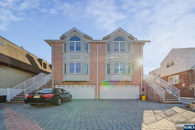 view of front of house with stairway, decorative driveway, brick siding, and an attached garage