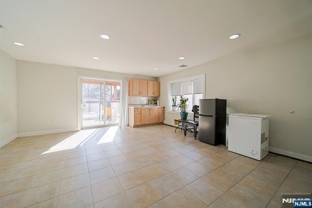 kitchen with light tile patterned floors, light brown cabinets, refrigerator, freestanding refrigerator, and light countertops