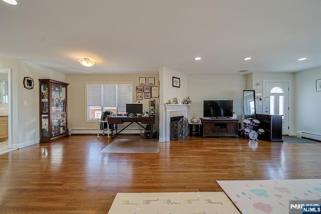 living room featuring a baseboard heating unit, plenty of natural light, and wood finished floors