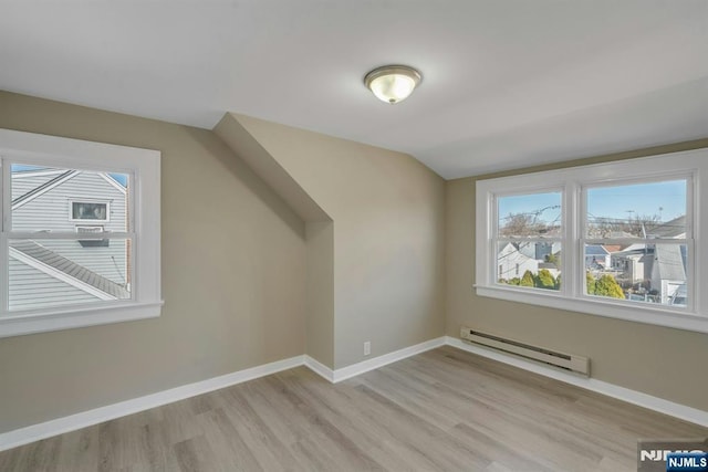 additional living space with light wood finished floors, a baseboard heating unit, baseboards, and vaulted ceiling