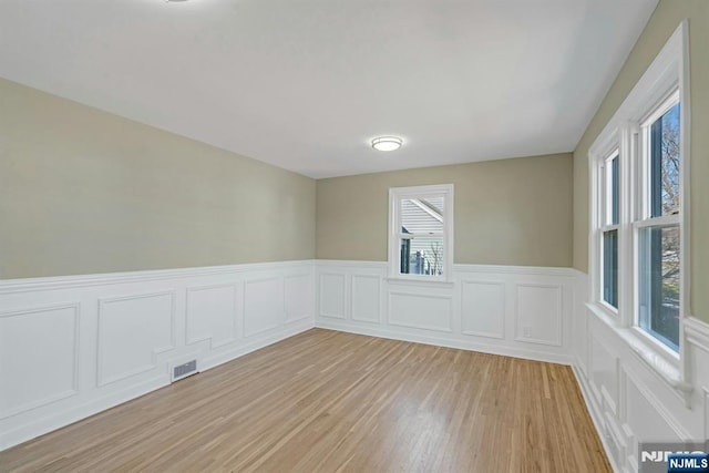 spare room with visible vents, light wood finished floors, and wainscoting