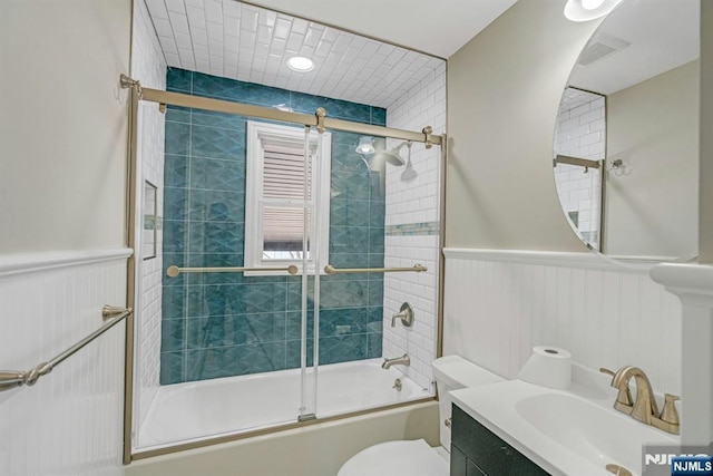 bathroom featuring vanity, toilet, a wainscoted wall, and bath / shower combo with glass door