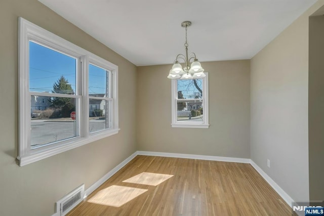 spare room with a notable chandelier, visible vents, light wood finished floors, and baseboards