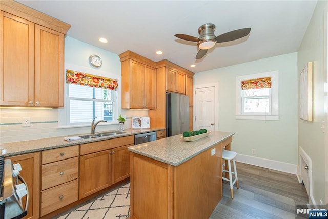 kitchen featuring a breakfast bar area, a ceiling fan, light stone countertops, a sink, and appliances with stainless steel finishes