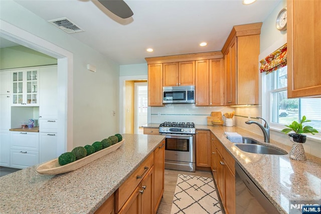 kitchen with light stone counters, visible vents, a sink, decorative backsplash, and stainless steel appliances