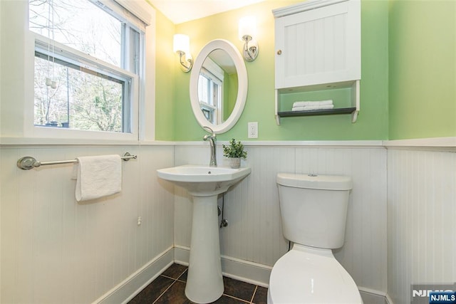 half bathroom with toilet, wainscoting, and tile patterned flooring