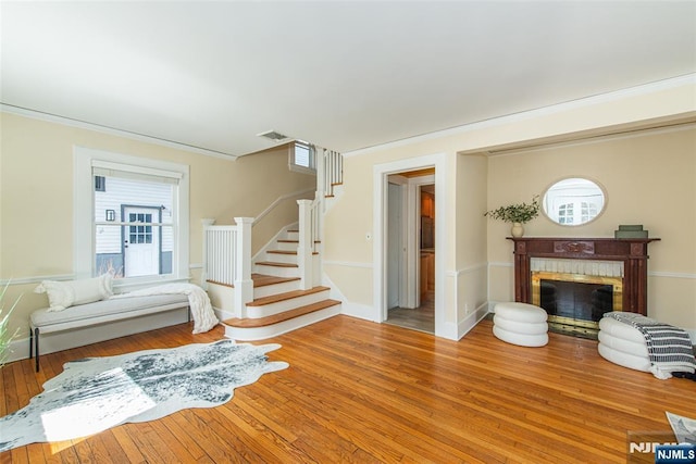 living room with light wood-style flooring, a fireplace, crown molding, baseboards, and stairs