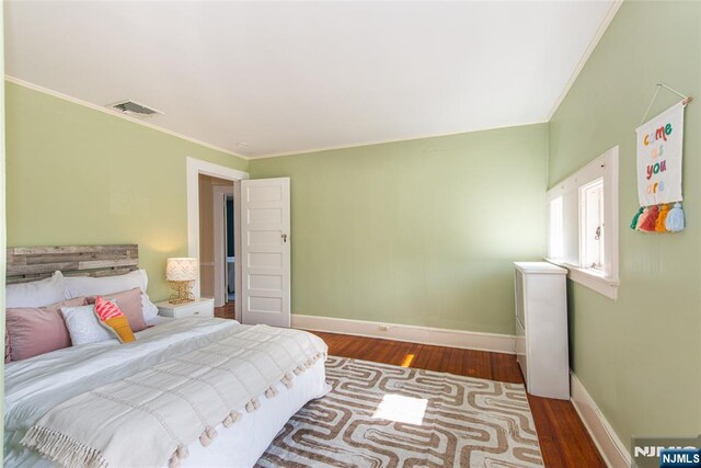 bedroom with visible vents, ornamental molding, baseboards, and wood finished floors