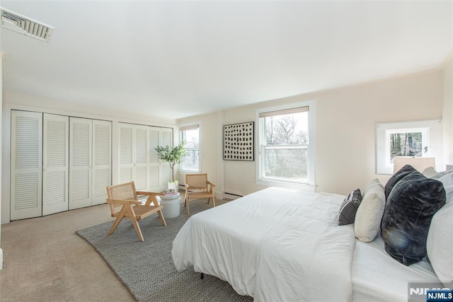 carpeted bedroom with visible vents, multiple closets, and a baseboard radiator