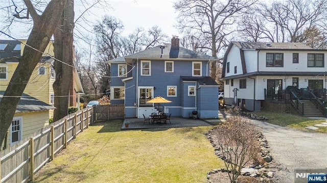 back of property with a patio, a fenced backyard, a lawn, and a chimney