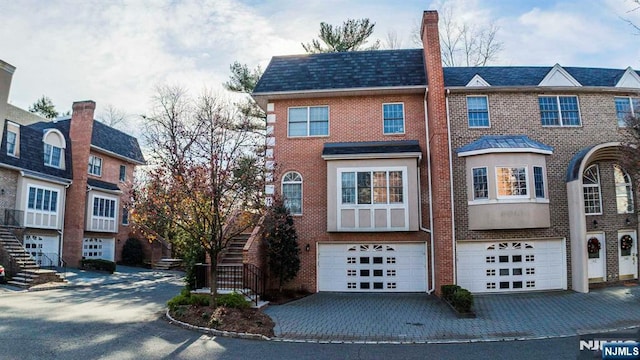 multi unit property with stairway, brick siding, a garage, and driveway