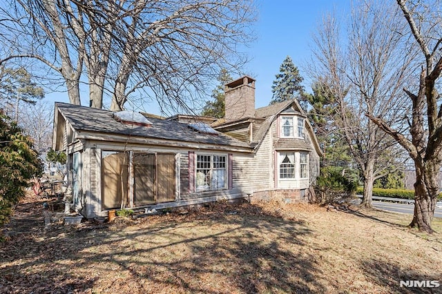 rear view of property featuring a gambrel roof and a chimney