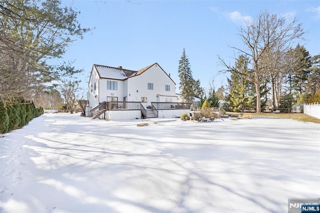 snow covered property featuring fence, a chimney, and a wooden deck