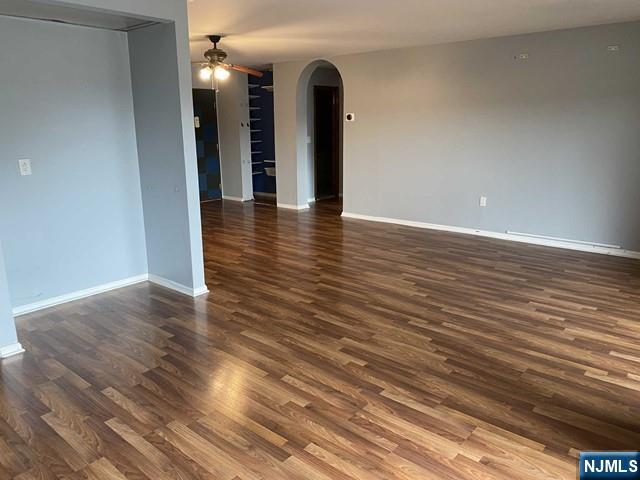 unfurnished room with arched walkways, baseboards, dark wood-type flooring, and ceiling fan